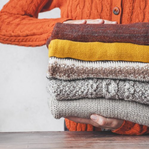 A,Woman,Holding,A,Stack,Autumn,Warm,Knitted,Sweaters.,Change