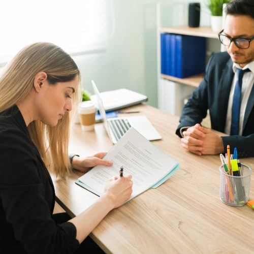 Beautiful caucasian woman signing a work contract to start a new job at a corporate office. Professional male boss making a business deal with a female client