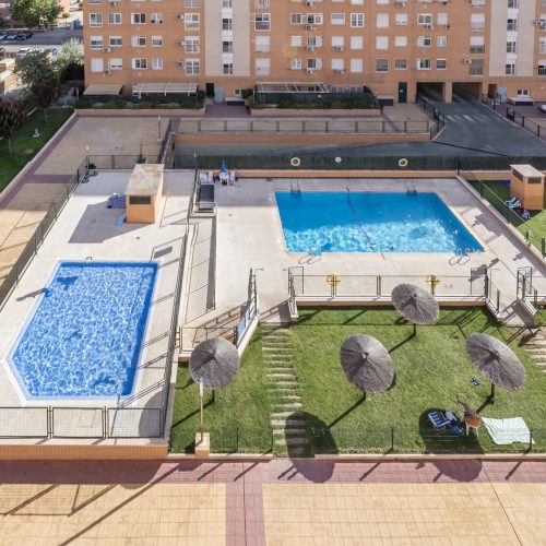 A pair of community pools with gardens, grass and wicker parasols in an urban housing development