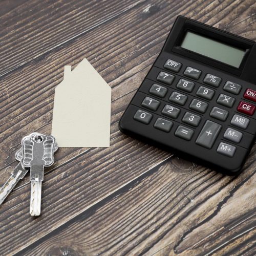 paper-cut-out-house-with-keys-calculator-wooden-textured-surface