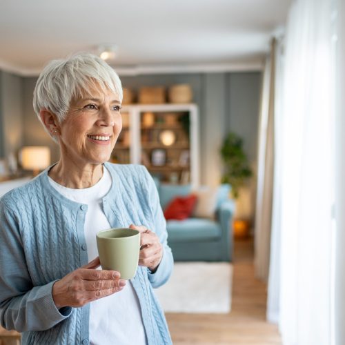 Happy,Senior,Woman,Holding,A,Mug,And,Looking,Out,The