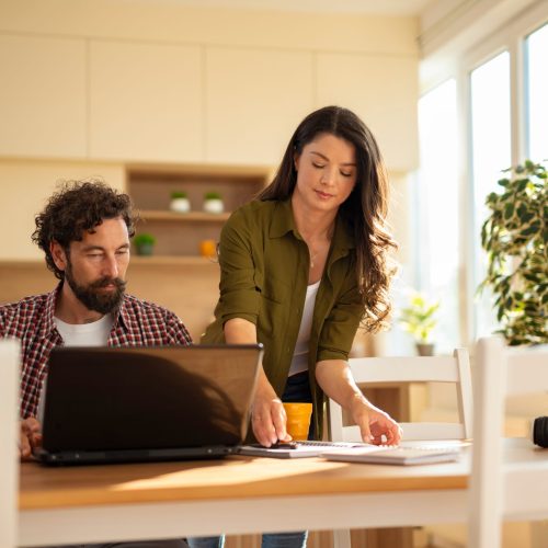 Young,Couple,Collaborating,At,Home,,Reviewing,Paperwork,And,Using,A