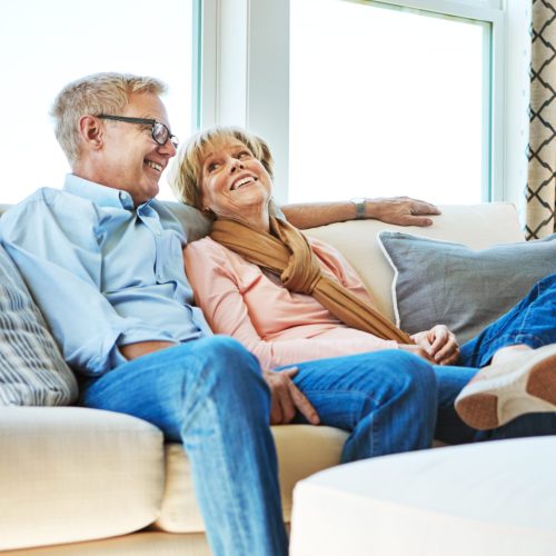 Talking, mature or happy couple in home to relax, enjoy conversation or joke together in retirement. Care, funny woman or senior man laughing with love, support or smile on house living room couch.