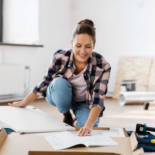 repair, improvement and furniture concept - happy smiling woman with manual assembling new locker at home