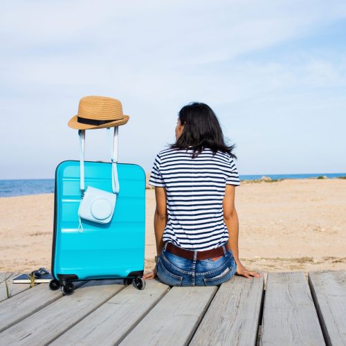young woman looking at the sea with her luggage